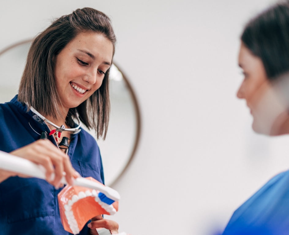 Two dental hygienists demonstrate a tooth brushing technique